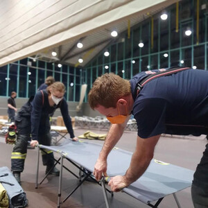 Eine Frau und ein Mann stellen ein Feldbett in der Eislaufhalle Germering auf. Foto mit Link zum Artikel