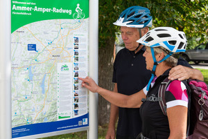 Foto: Zwei Radfahrer stehen vor einer Tafel mit der Karte des Ammer-Amper-Radwegs