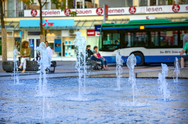 Foto zeigt Springbrunnen, im Hintergrund steht ein Bus an einer Bushaltestelle.