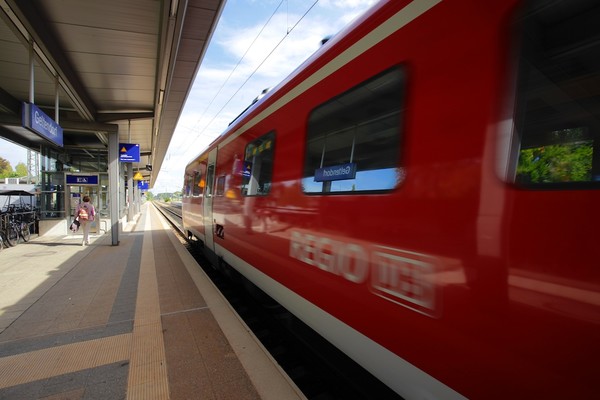 Roter Regionalzug fährt am Bahnsteig vorbei.