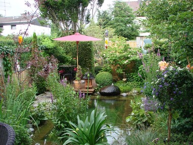 Foto: Garten mit Stauden, die einen Zierteich umgeben.
