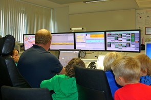 Foto Kinder besuchen die Integrierte Rettungsleitstelle und schauen zusammen mit einem Sachbearbeiter auf Monitore