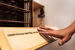 Foto: Finger gleiten über einen Holzbalken mit Braille-Schrift.