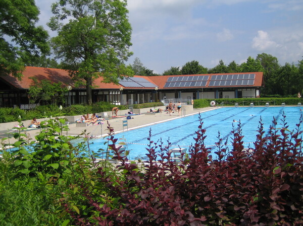 Schwimmbecken, dahinter eingeschossiges, L-fömiges Haus mit Umkleiden und Duschen
