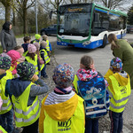 Kinder in gelben Warnwesten stehen vor Bus.