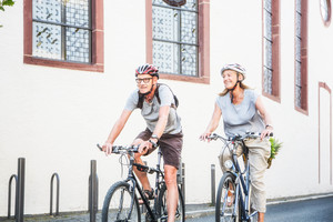 Foto zeigt zwei Radfahrer (Mann und Frau), die an einer Kirche vorbeifahren