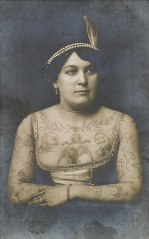 Oberkörper einer tatowierten Frau im Kleid.