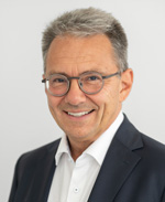Porträtfoto eines Mannes mit Brille im schwarzen Anzug ohne Krawatte